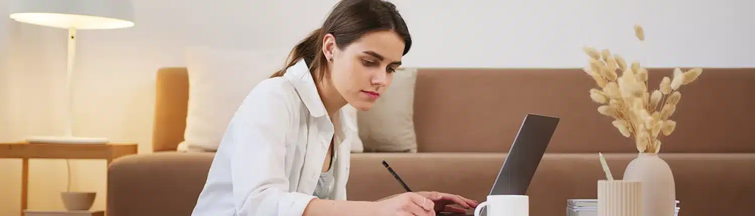 vrouw aan koffietafel aan het schrijven, laptop en kopje op tafel